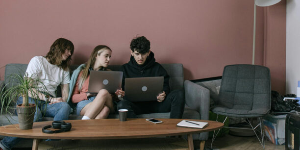 Group of young people sitting on gray couch working on separate laptops