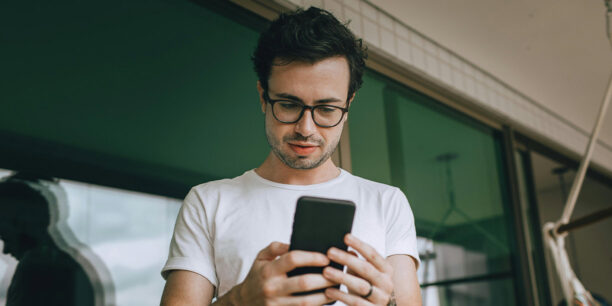 Man in white t-shirt typing on cell phone